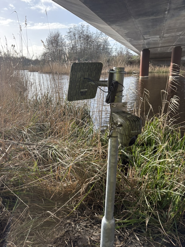 Camera en zonnepaneel onder een brug, naast het water.